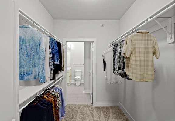 A white closet with clothes hanging on a rail.