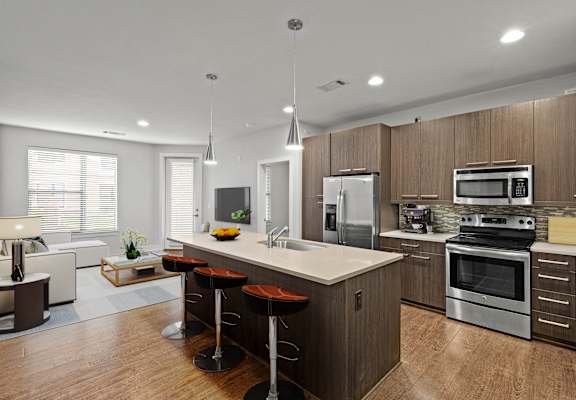 a modern kitchen with a large island with three bar stools and a living room