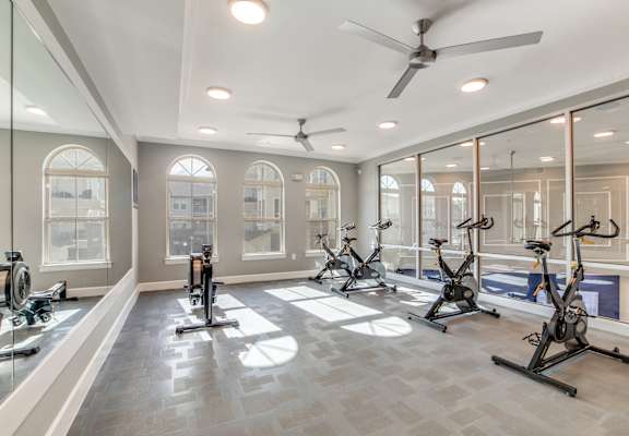 A spacious gym with a row of stationary bikes and a ceiling fan.