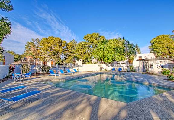 a swimming pool with blue chaise lounge chairs and trees in the background