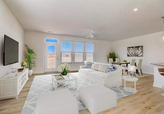 A living room with white furniture and a flat screen TV mounted on the wall.
