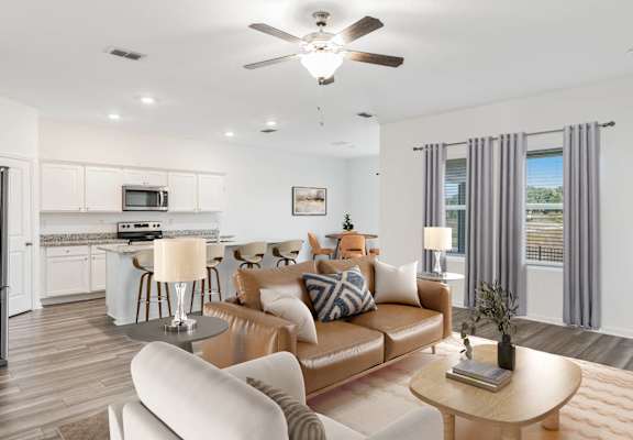 A modern living room with a brown leather couch and a white kitchen in the background.