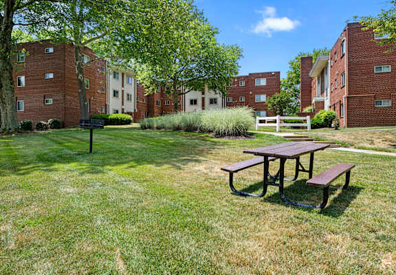 A picnic table sits in the middle of a grassy area in front of a brick building.