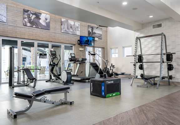 A gym with a variety of equipment including a weight bench, a treadmill, and a television.