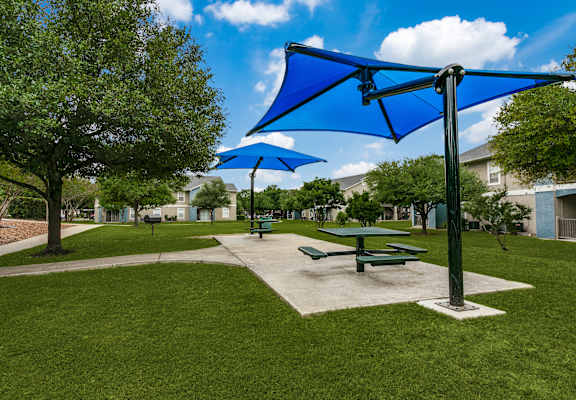 a picnic area with picnic tables and umbrellas at Rosillo Creek Apartments, San Antonio, TX
