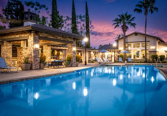 A swimming pool in front of a house with lights on.