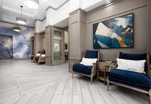 A modern living room with a blue couch and a large abstract painting on the wall.