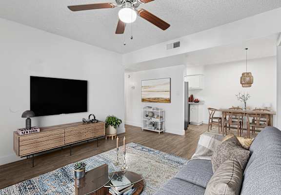 A living room with a grey sofa, a wooden coffee table, a flat screen TV, and a ceiling fan.