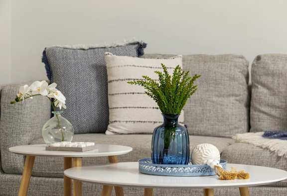 A living room with a grey couch, a white coffee table, and a blue vase with greenery.