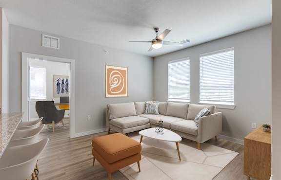 A living room with a white couch, a brown ottoman, and a ceiling fan.