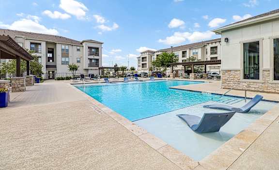 A swimming pool surrounded by lounge chairs and apartment buildings.