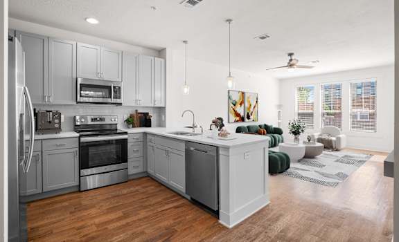 A modern kitchen with stainless steel appliances, pendant lighting, sleek cabinetry, hardwood floors, and a dishwasher and microwave.