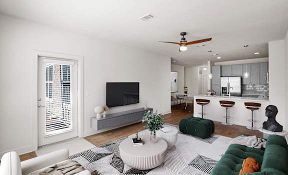 A living room with a ceiling fan, a balcony entrance door, hardwood floors, and barstool seating in the kitchen.