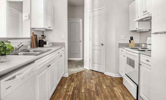 A white kitchen with wood floors and white appliances.