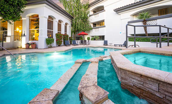 A swimming pool with a stone border and a building with a balcony in the background.