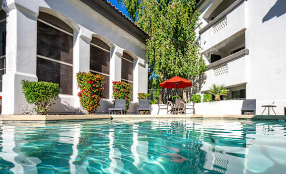 A pool with a red umbrella and chairs in front of a white building.