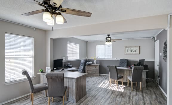 A room with a ceiling fan and a desk with chairs.
