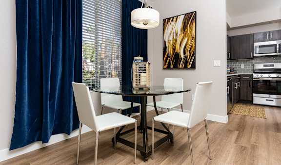 a dining area with a glass table and chairs and a window with a blue curtain