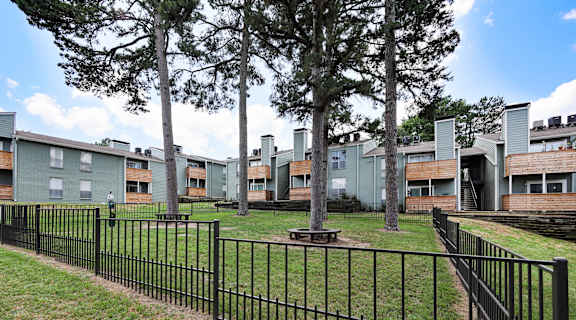 a grassy area with a picnic table and trees in front of an apartment complex
