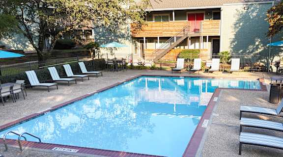a swimming pool with chairs and a building in the background