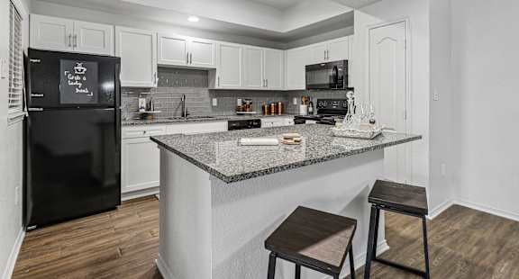 A kitchen with a black fridge and white cabinets.