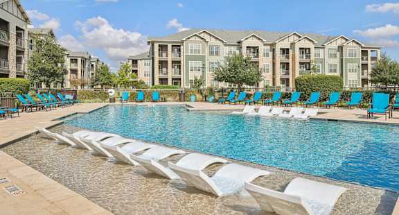 A swimming pool with lounge chairs and apartment buildings in the background.at North Creek, Hutto, TX, 78634