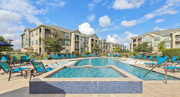 A large swimming pool surrounded by blue lounge chairs and apartment buildings in the background.at North Creek, Hutto, Texas