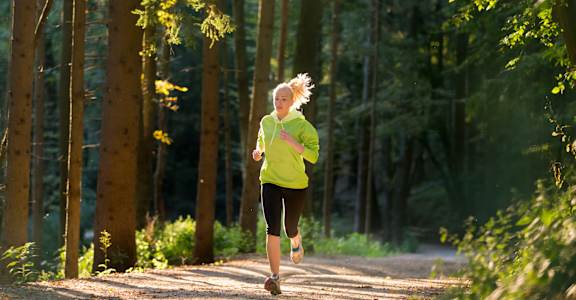 A woman in a yellow top and black pants is running on a path in a forest.