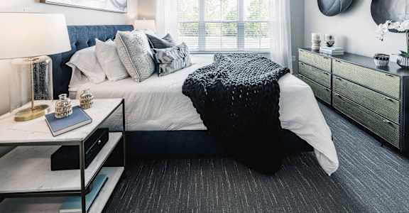 A bedroom with a large bed, a nightstand with a lamp, and a dresser with a mirror.