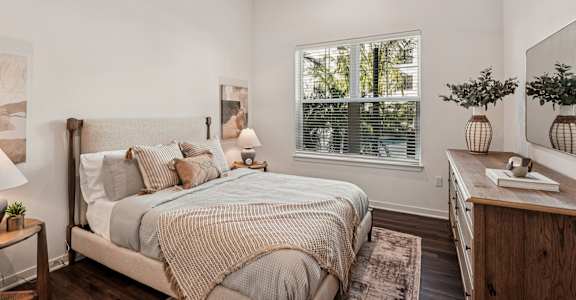 A bedroom with a bed, nightstand, and a window with blinds at The Stadler Luxury Apartments, Bradenton, FL