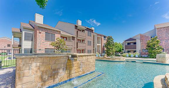 A swimming pool in front of a building with a stone wall.
