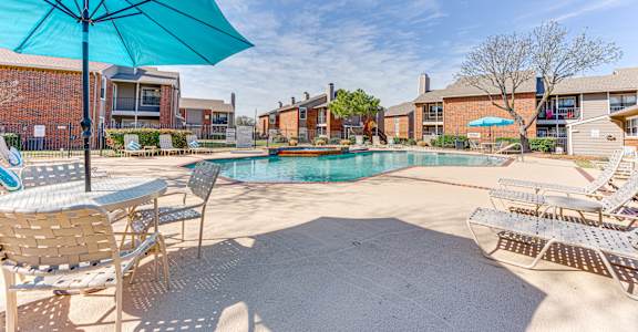 A pool area with a blue umbrella and chairs.