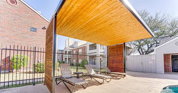 A wooden covered patio area with a pool and lounge chairs.