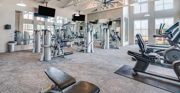 A gym with a variety of equipment including treadmills, weights, and a bench.