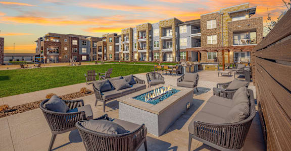A sunset view of a patio with chairs and a fire pit in front of apartment buildings at Magnolia Grove Apartments, Terrell, 75160