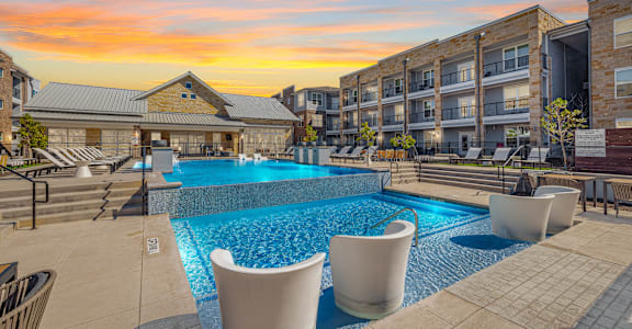 A swimming pool surrounded by lounge chairs in front of apartment buildings at Magnolia Grove Apartments, Terrell, 75160