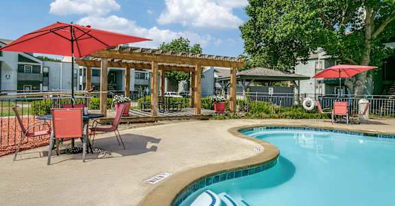 A pool with a red umbrella and chairs.