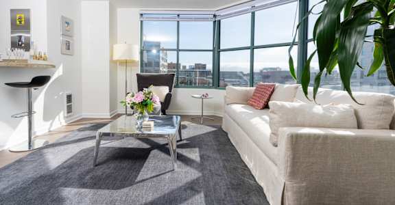 A living room with a white couch, a glass coffee table, and a large window.