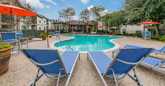 a swimming pool with blue chairs and umbrellas and apartments in the background at Sunrise Canyon, Universal City, TX, 78148