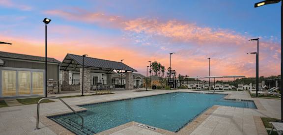 A swimming pool surrounded by a tiled patio and a building in the background.