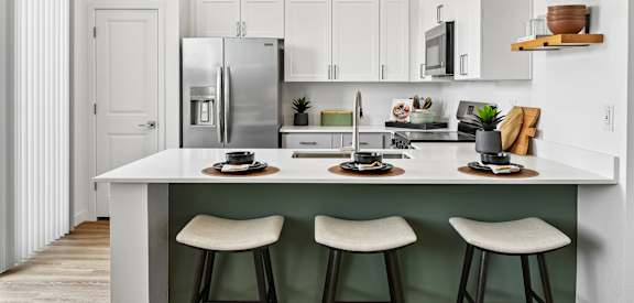 A kitchen with white cabinets and a white island with three stools.
