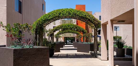 a covered walkway between two buildings with plants and trees