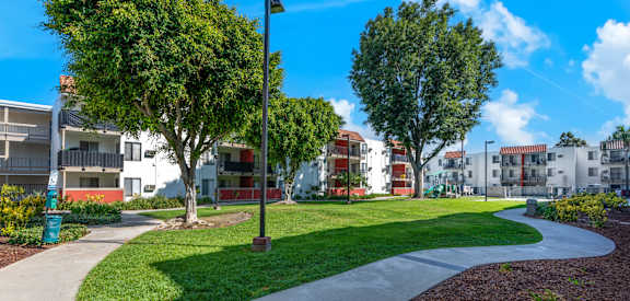 a park with grass and trees in front of apartment buildings