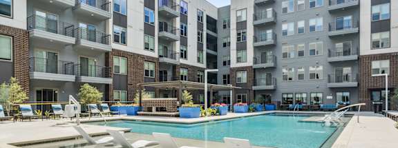 an apartment swimming pool with chairs in front of an apartment building