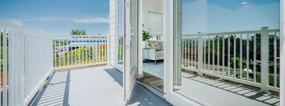 A white balcony with a glass door leading to a patio.