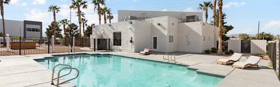 A swimming pool in front of a house with a fence and palm trees.