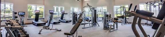 A spacious gym with a variety of equipment and a ceiling fan.