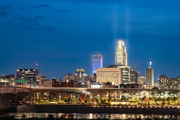 A city skyline at night with a bridge crossing a river in the foreground.