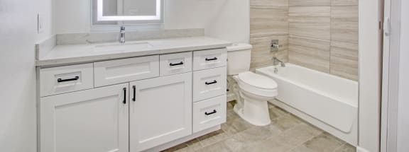 a bathroom with white cabinets and a white toilet next to a white bathtub with a shower