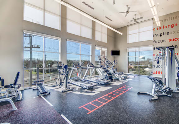 a gym with cardio machines and windows with a view of the city